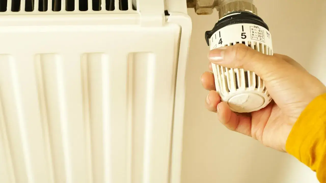 Mano ajustando el termostato de un radiador para controlar la potencia.