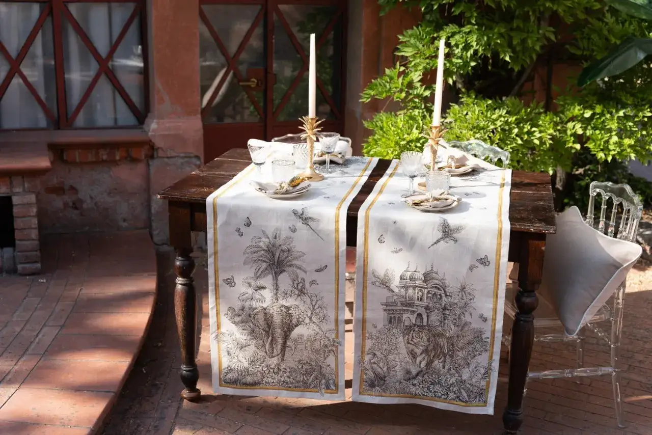 Tavolo rettangolare apparecchiato con runner decorato con elefanti e tigri, candelabri dorati e bicchieri. Idee per cosa mettere su un tavolo rettangolare.