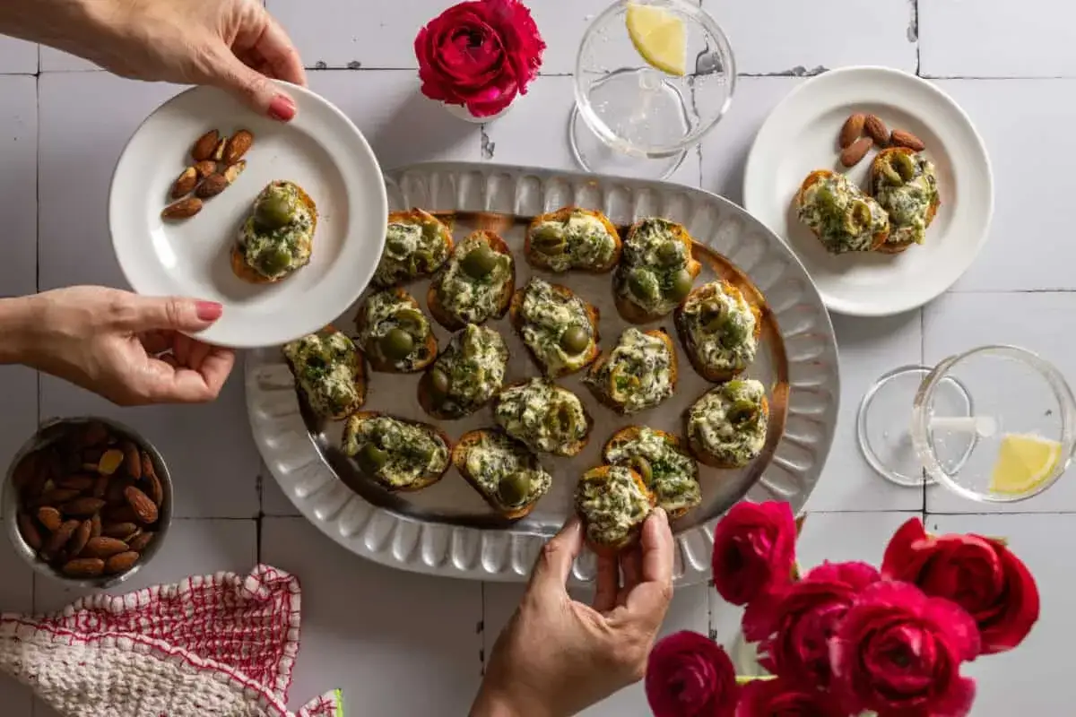 K&ouml;stliche Bruschetta mit Olivencreme, perfekt f&uuml;r ein einfaches olivencreme rezept. Mandeln und Blumen garnieren die Szene.