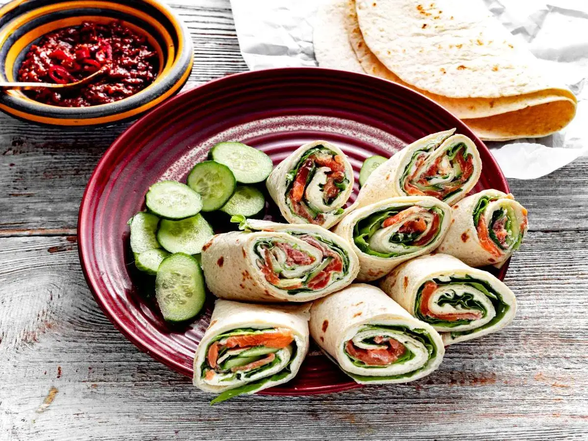 Pyszna tortilla z łososiem, świeżym ogórkiem i sałatą, podana na talerzu z dodatkiem sosu.