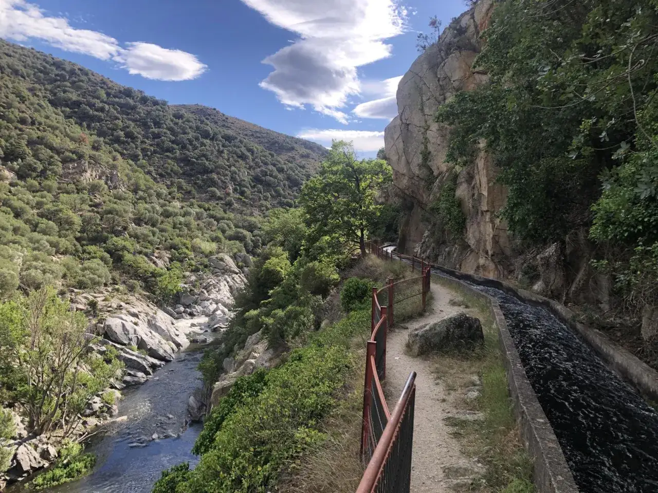Sentier longeant un canal d'eau vive dans les gorges de la Guillera, avec une rivi&egrave;re en contrebas et des montagnes verdoyantes.
