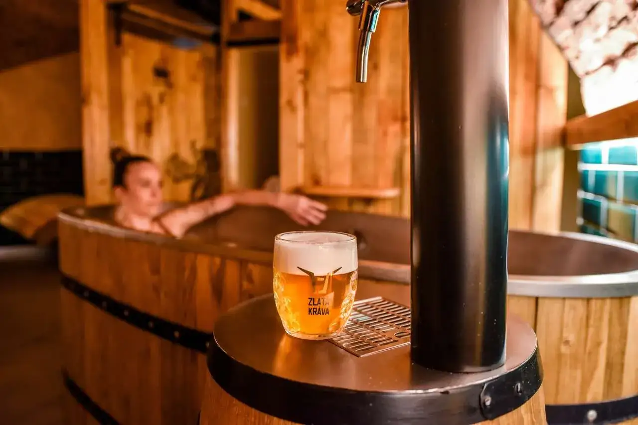 Entspannung im Pilsen Bierhotel: Eine Frau genie&szlig;t ein Bad in einem Bierfass, w&auml;hrend ein k&uuml;hles Pils daneben zapfbereit steht.