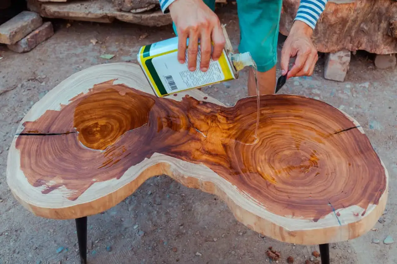 Application d'essence de térébenthine sur une table en bois brut pour en révéler la beauté naturelle.