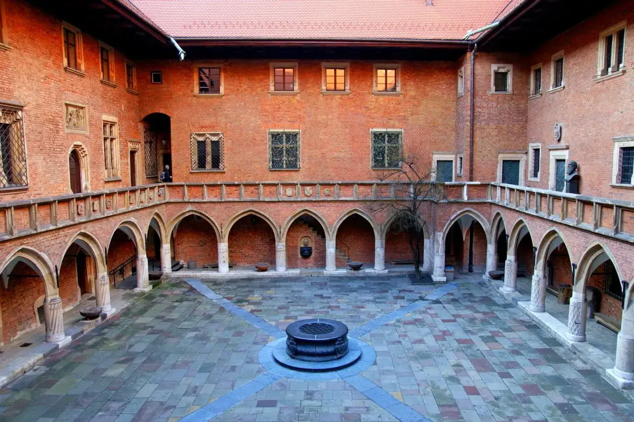 Dziedziniec Collegium Maius w Krakowie z arkadowymi krużgankami, studnią i ceglanymi murami.