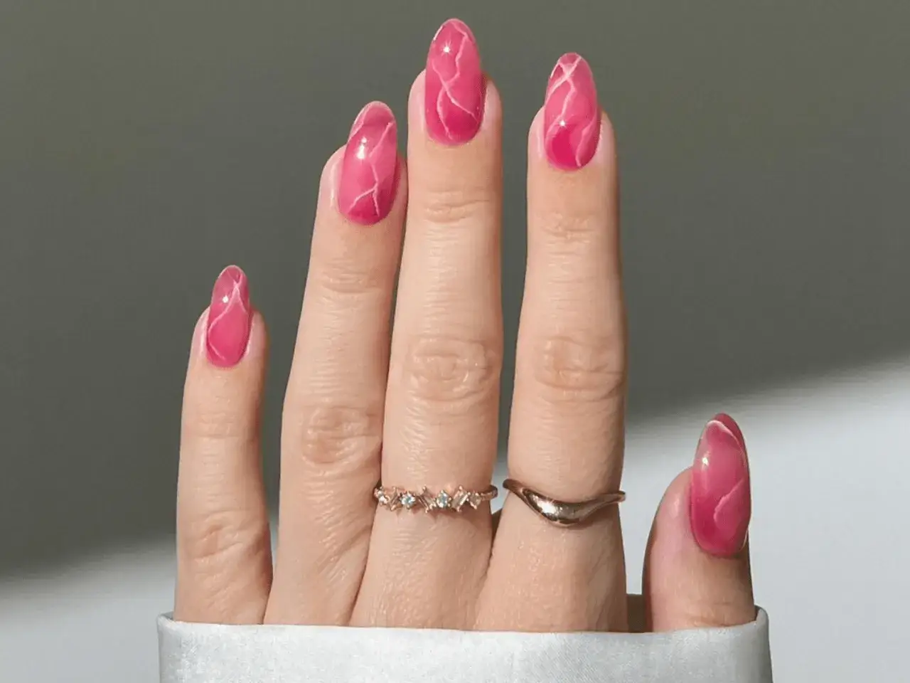 Vacker hand med mandelformade naglar i rosa nagellack med marmorering. Tv&aring; tunna ringar pryder fingrarna.
