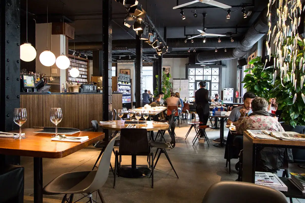 Mesas listas para disfrutar de sitios chulos para cenar en Madrid baratos. Ambiente moderno con luces colgantes y plantas.