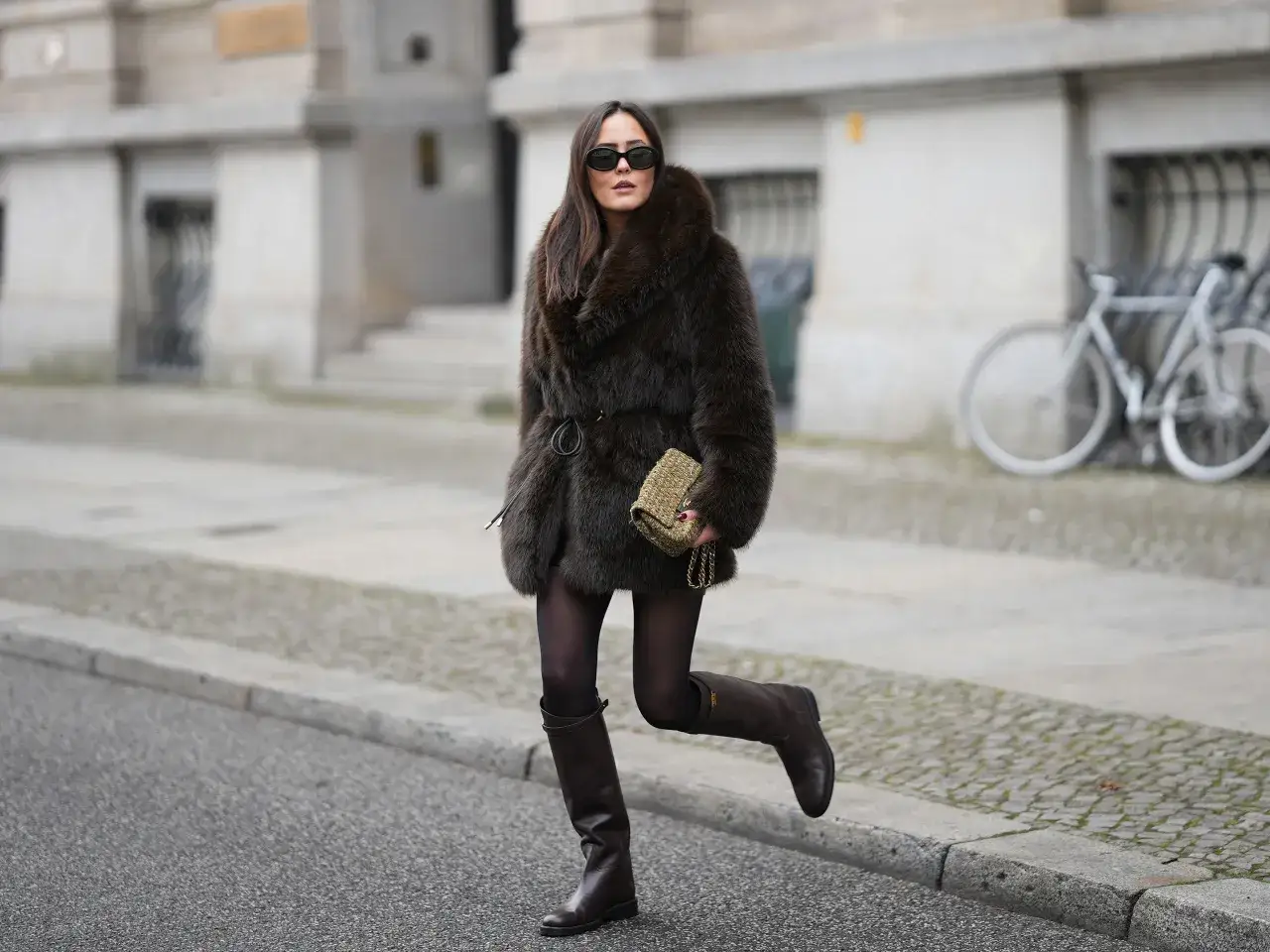 Donna con cappotto di pelliccia marrone, occhiali da sole e stivali alti in pelle marrone, un esempio di come indossare gli stivali alti con stile.