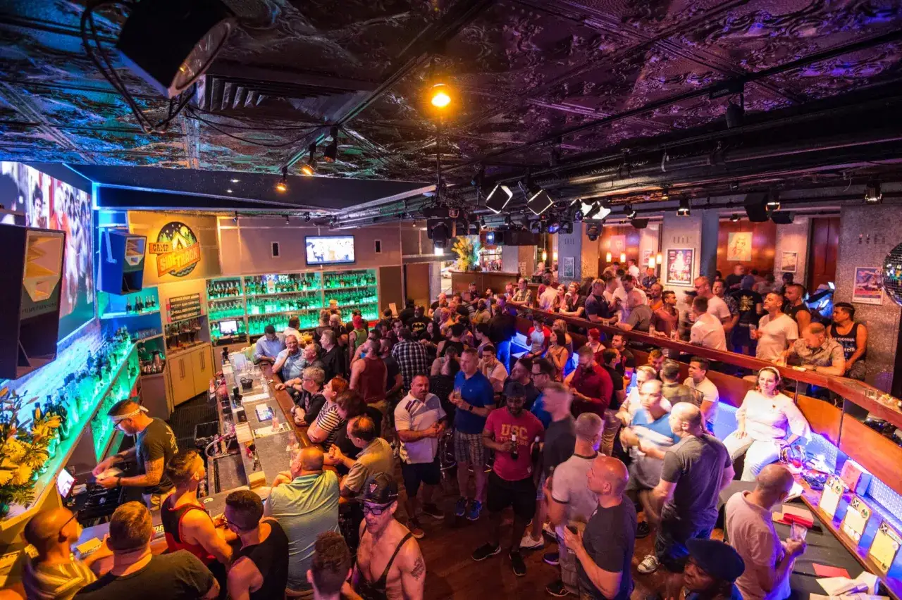 A lively crowd fills a bar, with a bartender serving drinks. This vibrant scene captures the energy of one of the best gay bars in Chicago.