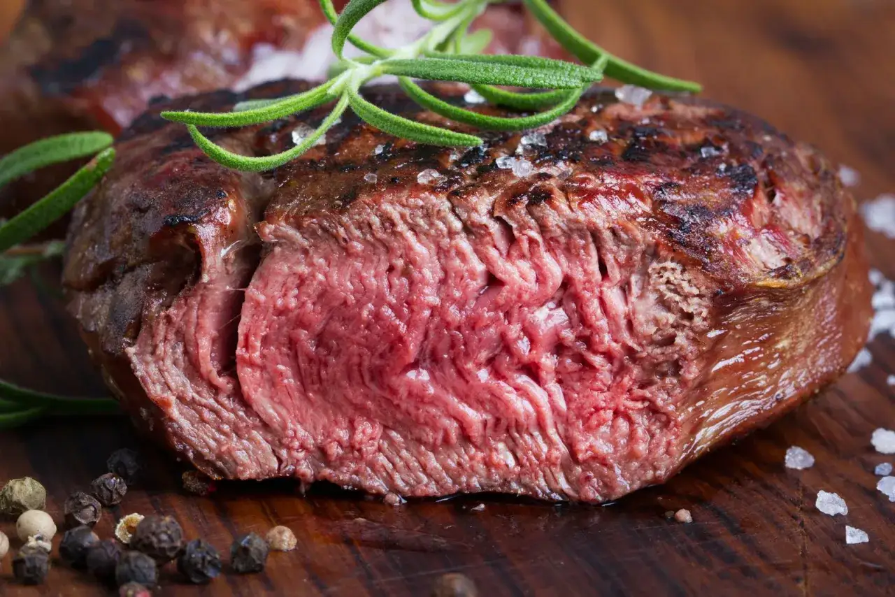 Succulenta tagliata di manzo al sangue, guarnita con rosmarino fresco e pepe nero su tagliere di legno.