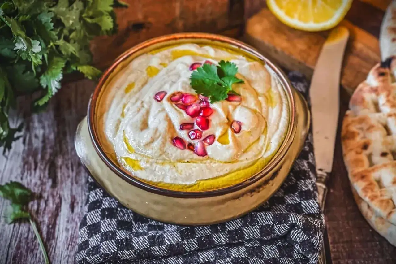 Cremiges Baba Ganoush, garniert mit Granatapfelkernen und Koriander, daneben Fladenbrot und Zitrone.