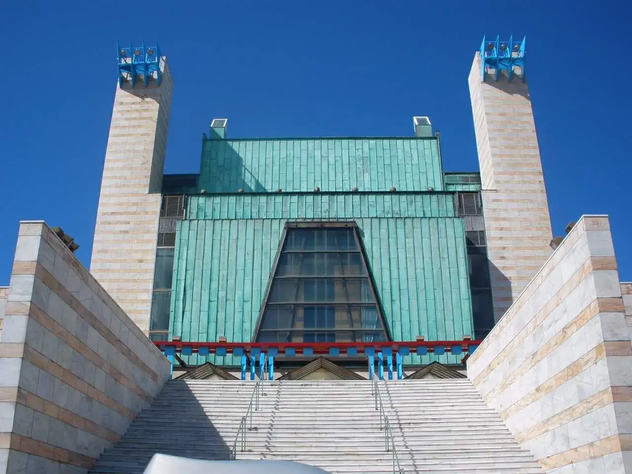 El **palacio de festivales** se alza majestuoso con sus torres de mármol y tejado verde. Escaleras blancas conducen a su entrada.