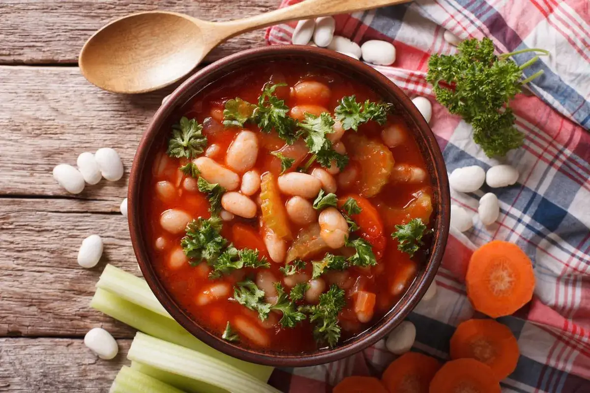 Zuppa di fagioli in umido con pomodoro e prezzemolo, perfetta se si possono cuocere all'uccelletto. Accanto, ingredienti freschi e un cucchiaio di legno.