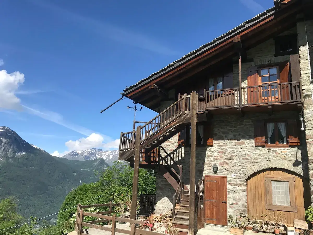 Maison de montagne en pierre avec escalier ext&eacute;rieur en bois, offrant une vue imprenable sur les Alpes. Id&eacute;al pour une location vacances Aoste, Italie.