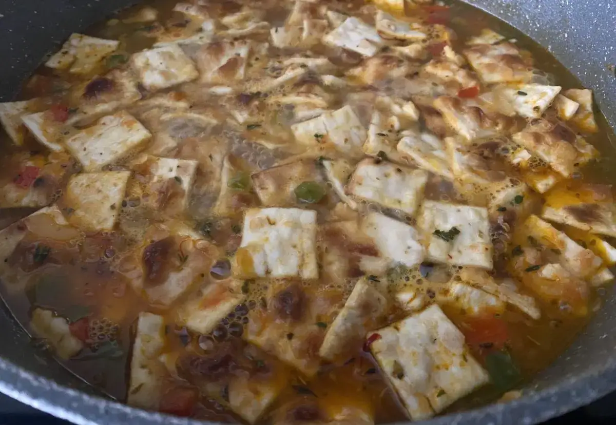 Gazpacho de mero Santa Pola hirviendo en una sartén, con trozos de pan y verduras.