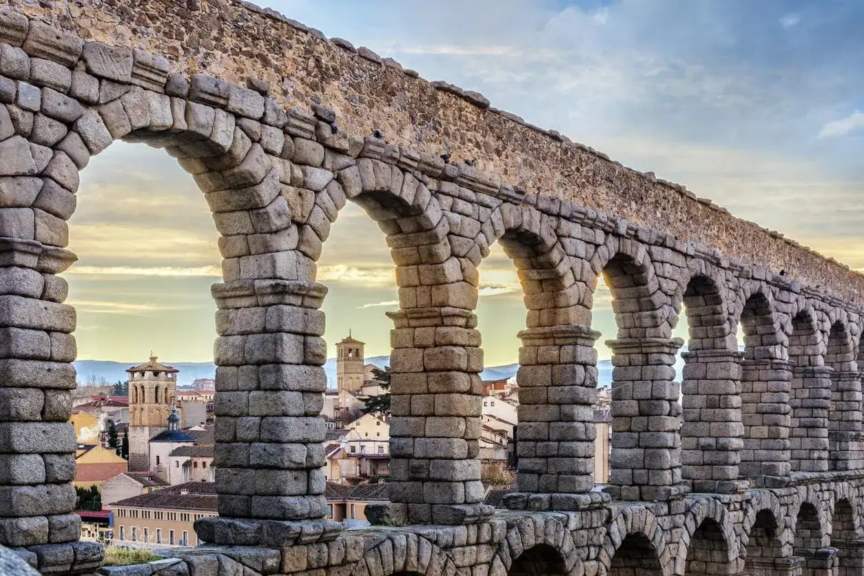 Acueducto romano de Segovia, un vestigio de la romanizaci&oacute;n de la pen&iacute;nsula ib&eacute;rica, con arcos de piedra y la ciudad al fondo.
