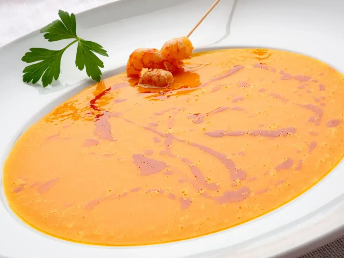 Crema de calabaza naranja, ideal para recetas saludables. Decorada con gambas y perejil.