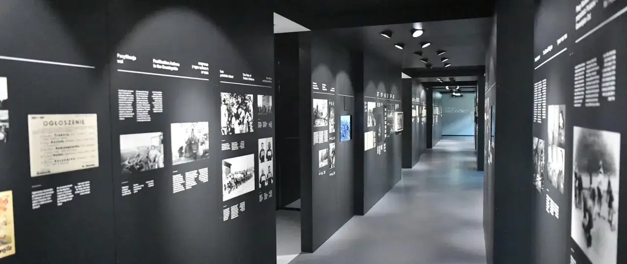 Wystawa w muzeum opowiadająca o obozie w Auschwitz. Czarno-białe fotografie i teksty na ciemnych ścianach korytarza.