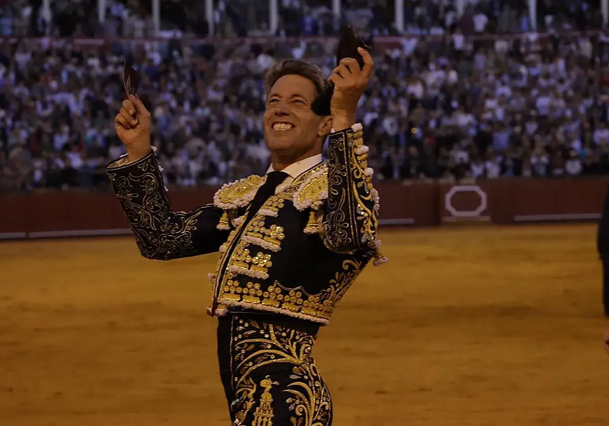 Manuel Escribano, torero con traje de luces, levanta las orejas de un toro ante una multitud.