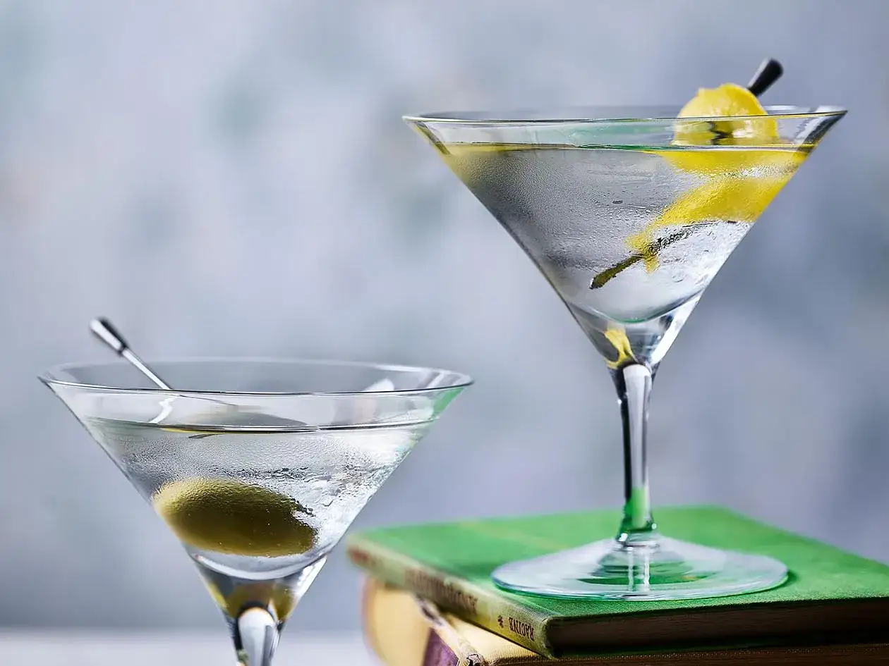 Deux verres de cocktail martini, l'un avec une olive, l'autre avec un zeste de citron, posés sur des livres.