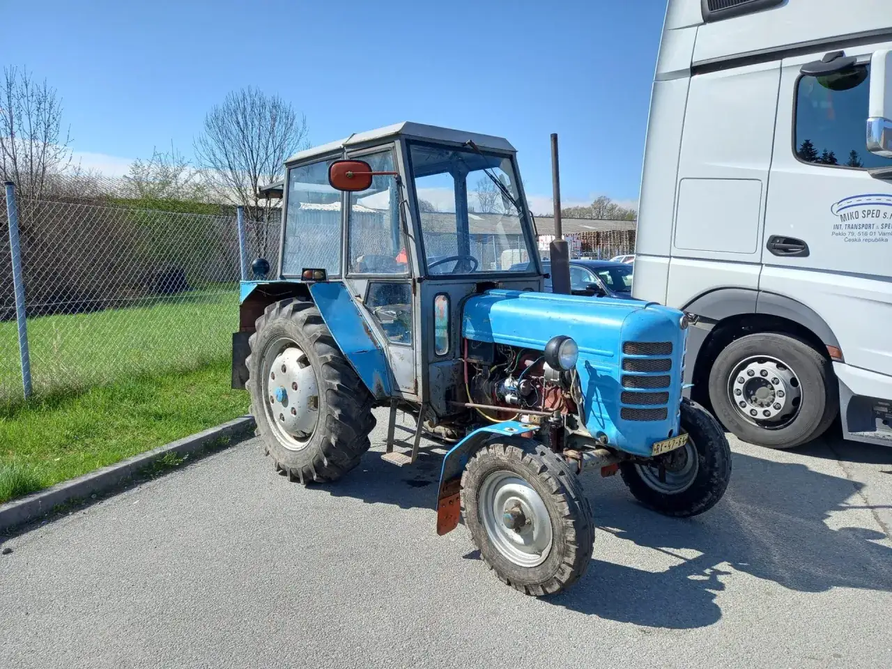 Zetor 3011, niebieski ciągnik z kabiną, stoi obok białej ciężarówki.
