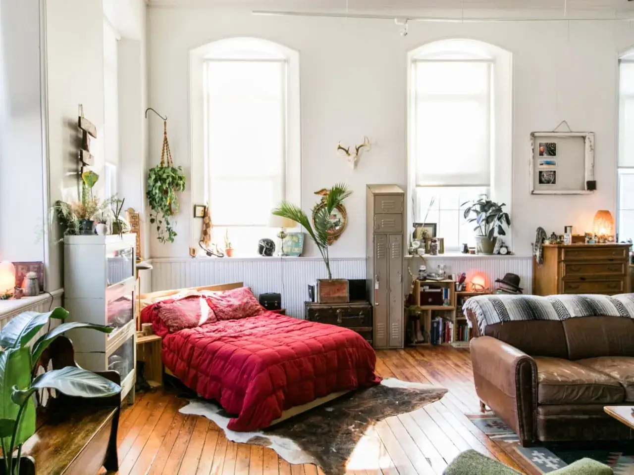 Un lit rouge et un canap&eacute; brun cr&eacute;ent deux zones distinctes, comme pour s&eacute;parer une petite chambre en deux. Des plantes et des objets d&eacute;co ajoutent du caract&egrave;re.