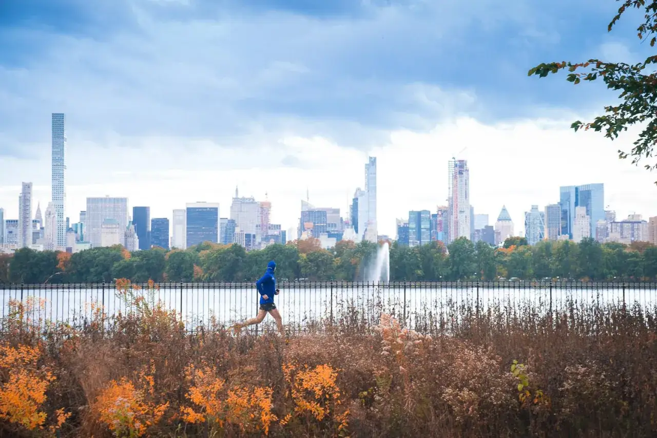 Läuferin im blauen Hoodie genießt die frische Luft, egal ob morgens oder abends joggen, mit Blick auf die Skyline von New York City.