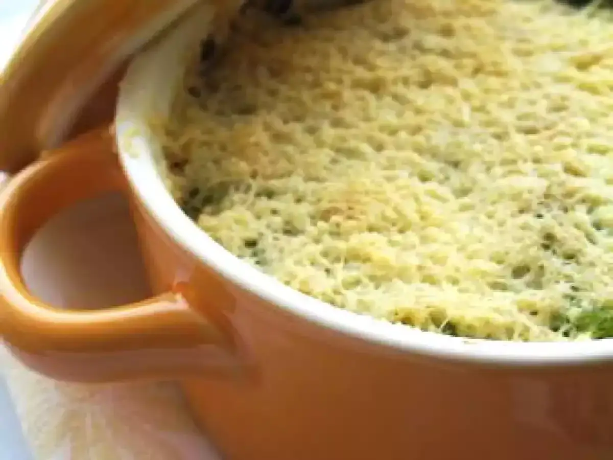 Un plat gratiné de purée de brocolis, doré et appétissant, dans une cocotte orange.