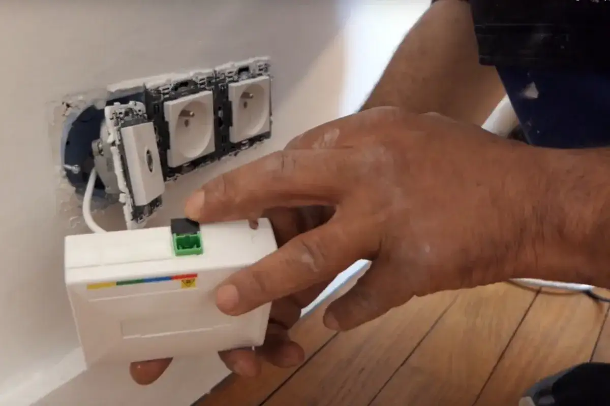 Installation d'une prise fibre optique murale. Une main tient un bo&icirc;tier blanc, pr&ecirc;t &agrave; &ecirc;tre connect&eacute; aux prises &eacute;lectriques. Avoir la fibre sans box, c'est possible !