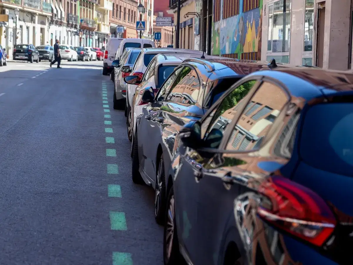 L&iacute;nea verde en el asfalto indica la diferencia entre zona azul y zona verde de aparcamiento. Coches aparcados en la calle.