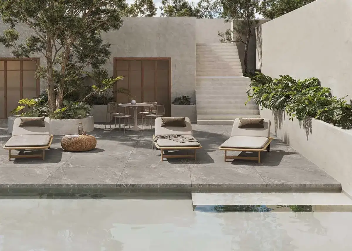 Terraza moderna con tumbonas y piscina. El suelo de baldosas grises, con una **norma resbaladicidad C1, C2, C3**, ofrece seguridad y estilo.