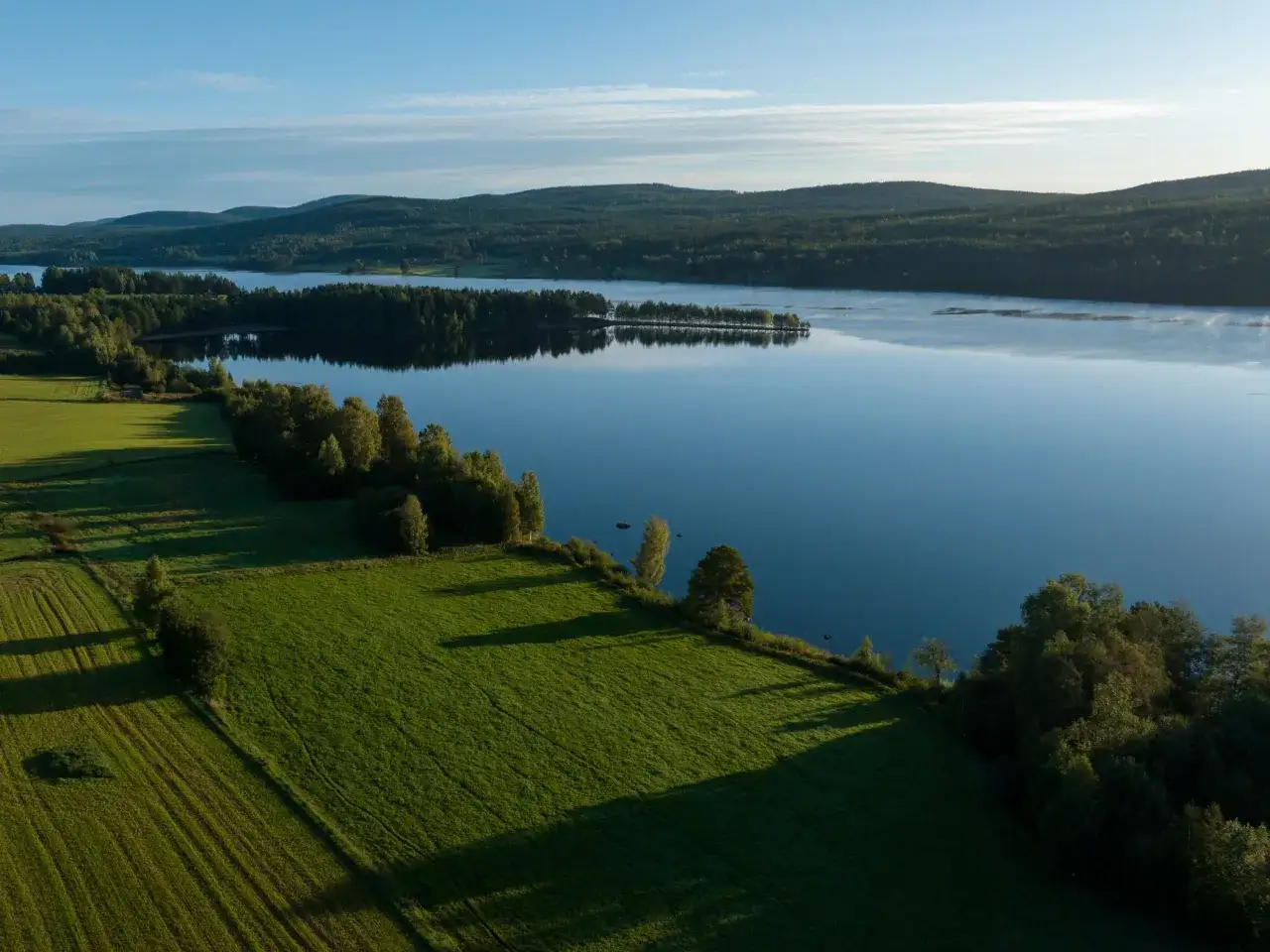 Gr&ouml;nskande f&auml;lt m&ouml;ter en spegelblank sj&ouml; vid STF Undersvik. Skogskl&auml;dda kullar str&auml;cker sig mot en klarbl&aring; himmel.