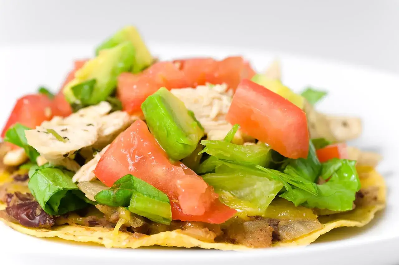 En närbild på en läcker tostada de pollo med kyckling, tomat, avokado och sallad.