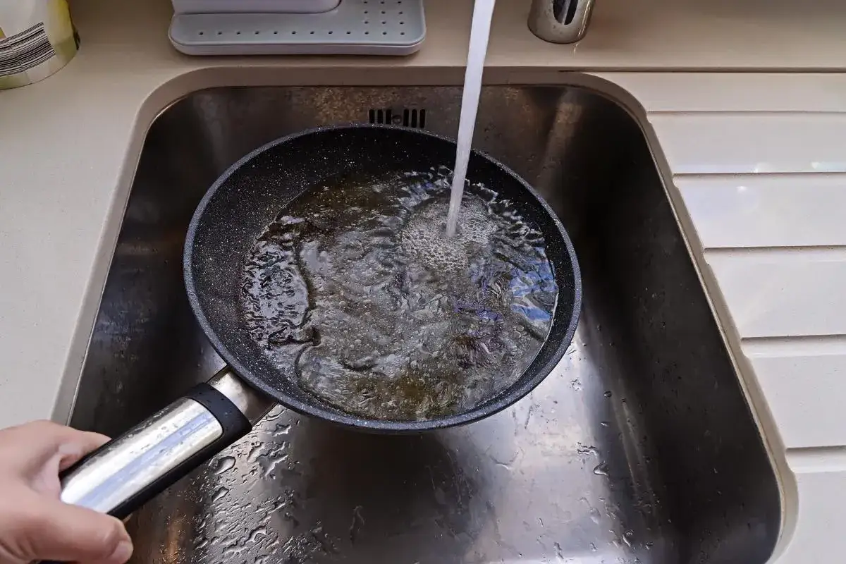 Une poêle sale sous l'eau courante. Une méthode pour comment enlever une tache de brulure.
