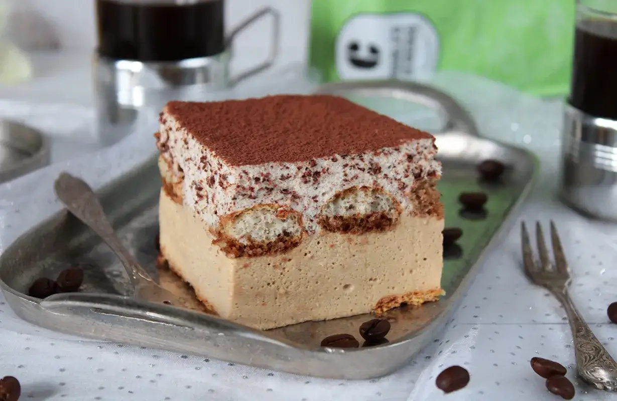 Pyszne ciasto cappuccino z mascarpone, posypane kakao, na srebrnej tacy z kawowymi ziarnami. Idealne na deser.