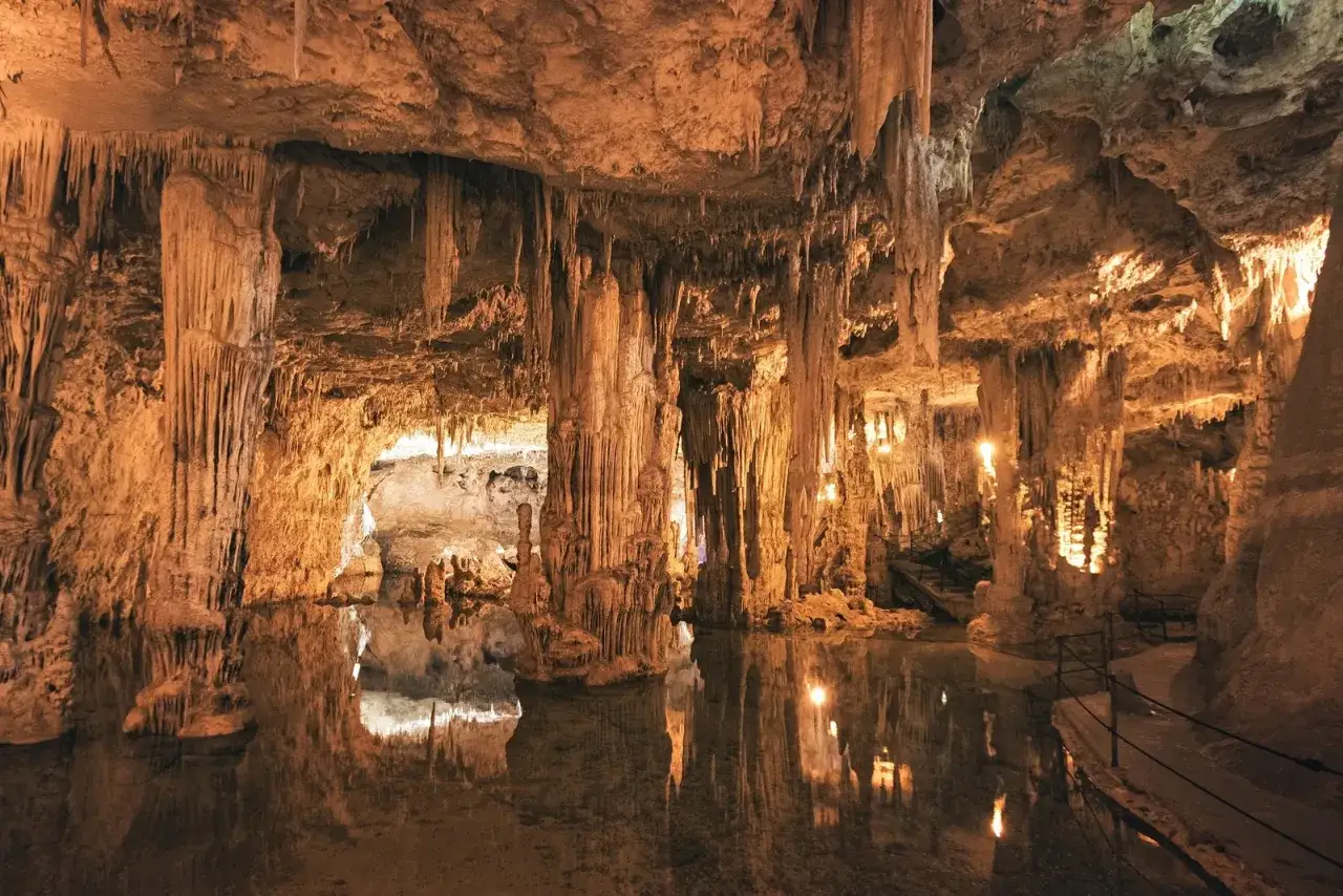 Grotta di Nettuno: un'esperienza magica per scoprire cosa fare ad Alghero. Stalattiti e stalagmiti creano un paesaggio surreale riflesso sull'acqua.