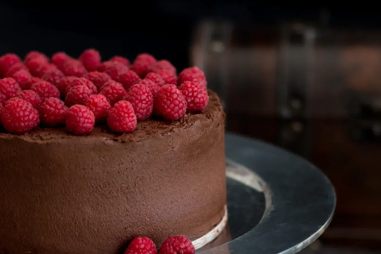 Schokokuchen rezept: Ein saftiger Schokoladenkuchen, üppig mit frischen Himbeeren belegt, auf einer silbernen Platte.