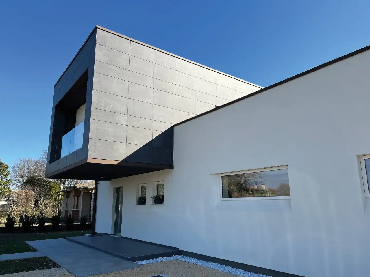 Moderna casa con facciata ventilata pro e contro: un blocco grigio rivestito in lastre si affaccia su una parete bianca con finestre.