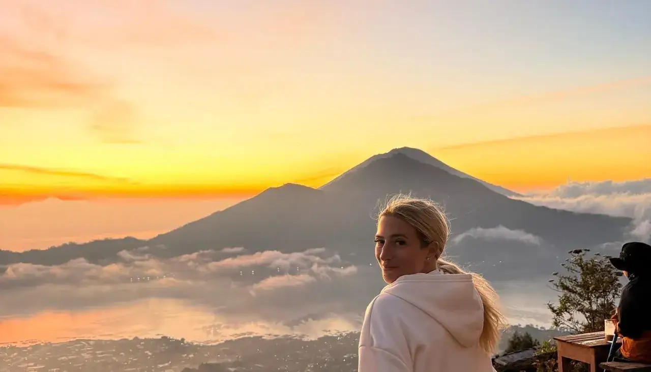 Mujer rubia disfruta un amanecer espectacular en su viaje a Indonesia 15 días. Montañas y nubes cubren el paisaje.