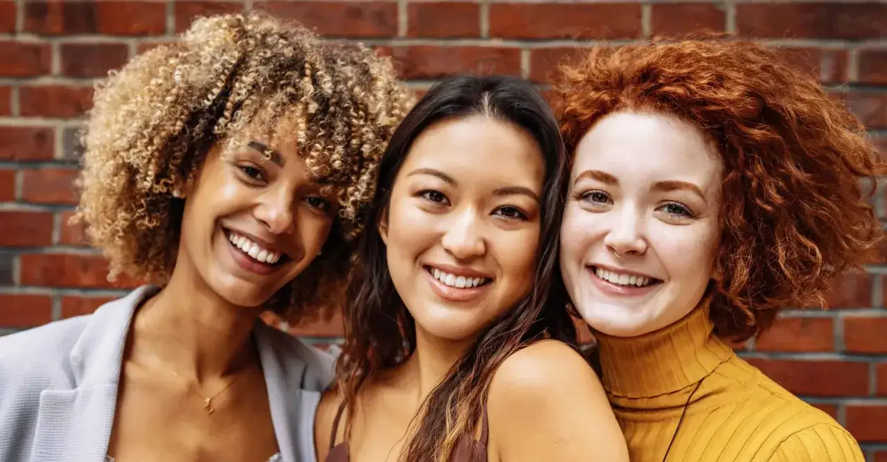 Drei l&auml;chelnde Frauen mit unterschiedlichen, tollen haar styles: blonde Locken, glattes dunkles Haar und rote Wellen.