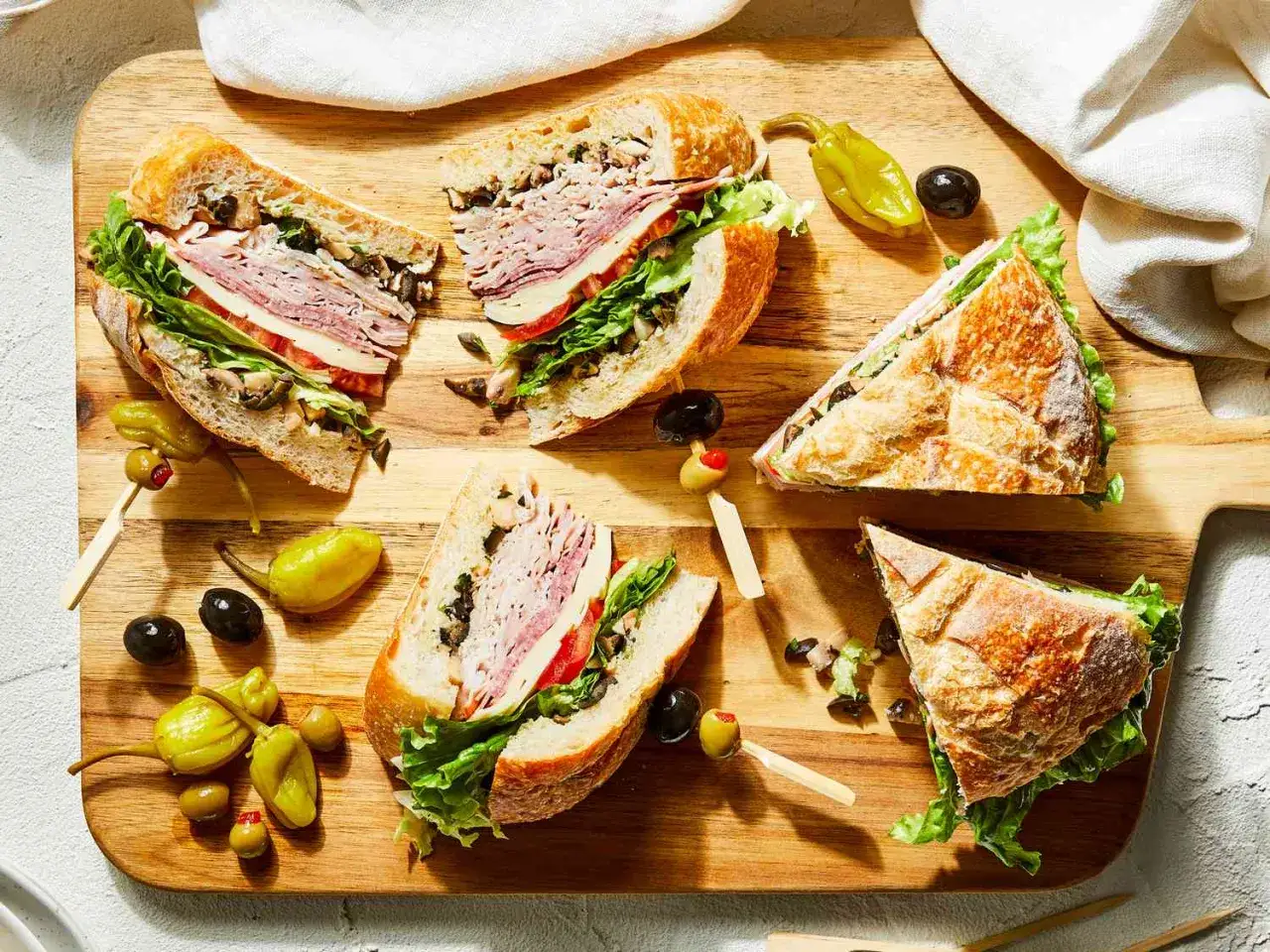 En h&auml;rlig italiensk macka, uppdelad i bitar, med k&ouml;tt, ost, sallad och oliver p&aring; en tr&auml;sk&auml;rbr&auml;da.