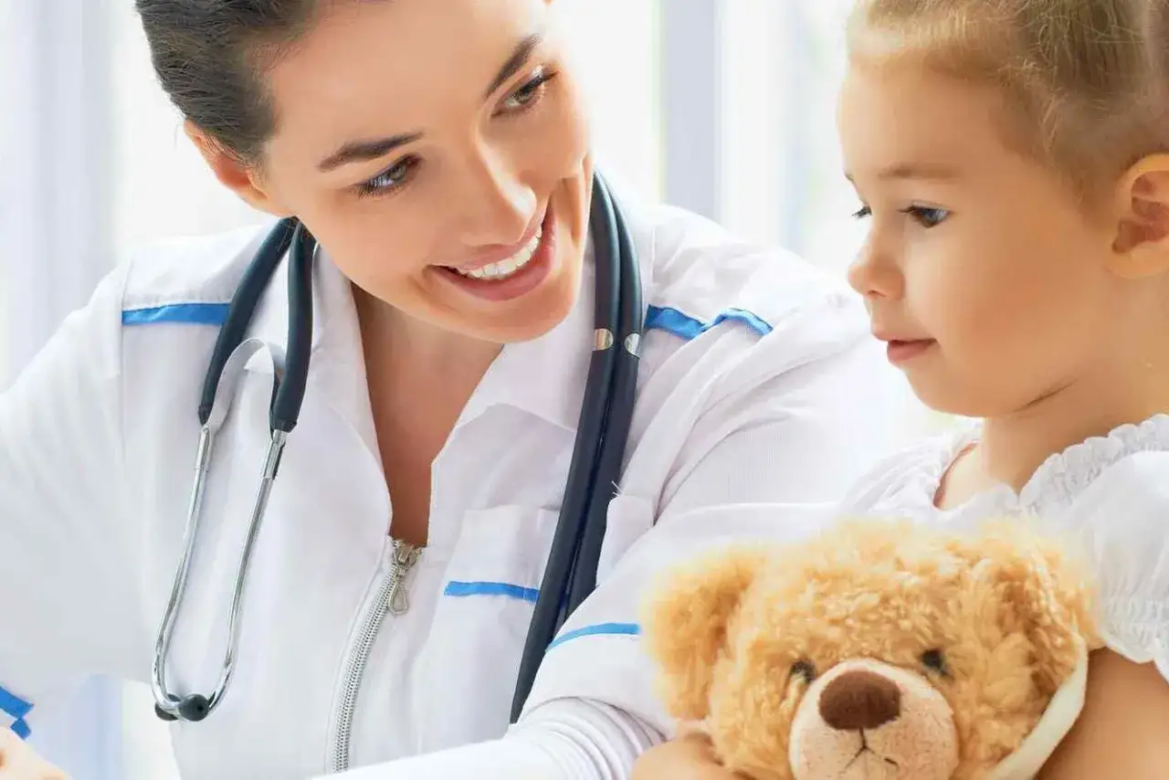 Un neuropsichiatra infantile sorride a una bambina con un orsacchiotto. La professione è gratificante, ma quanto guadagna un neuropsichiatra infantile?