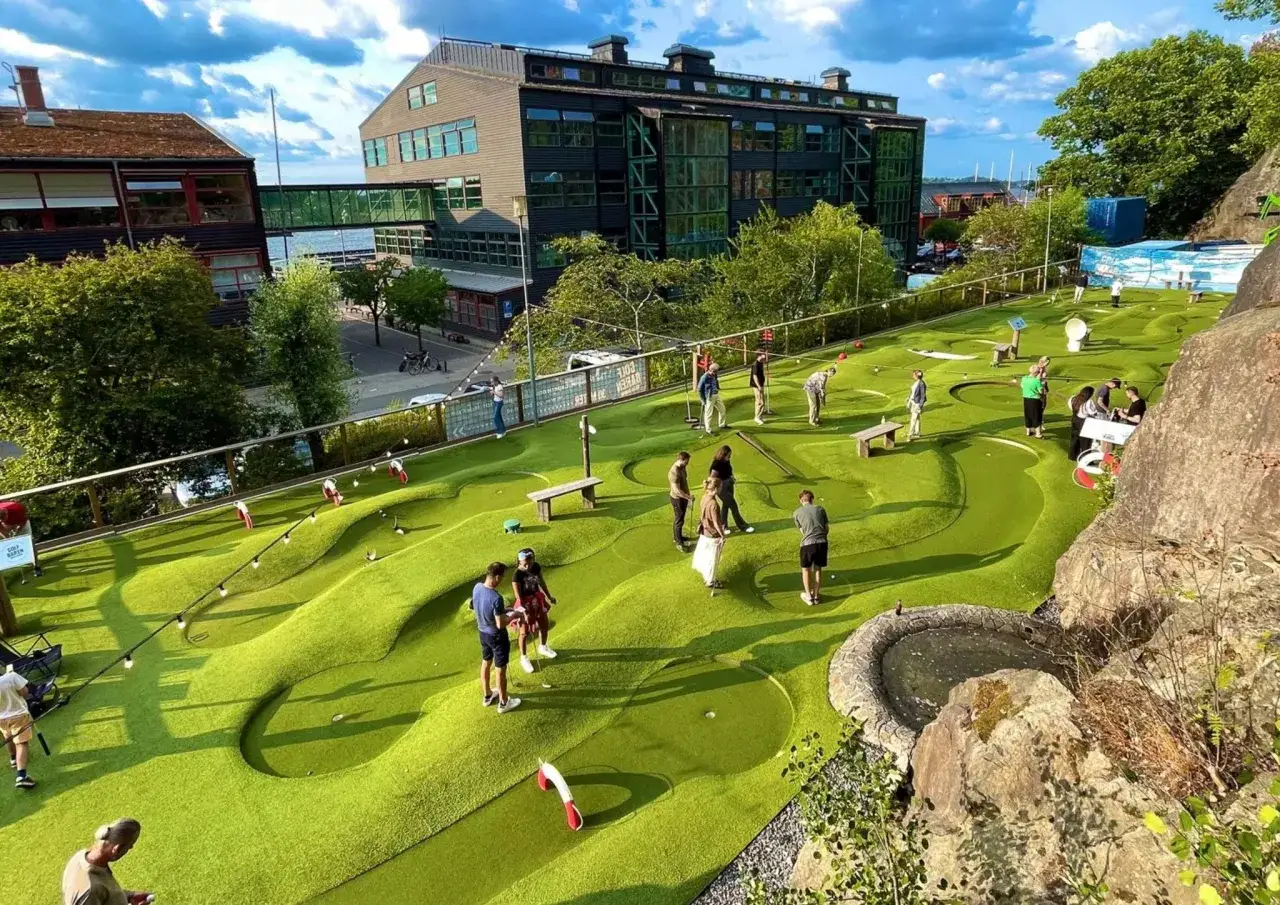 Grönt minigolf i Nacka Strand med folk som spelar. En solig dag med moln på himlen.