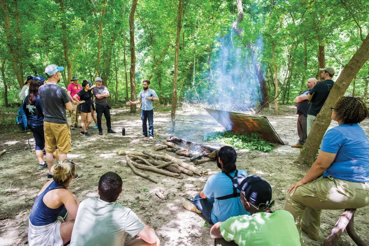 Grupa ludzi uczy się, co to bushcraft, podczas warsztatów w lesie. Instruktor pokazuje, jak rozpalić ognisko i zbudować schronienie.
