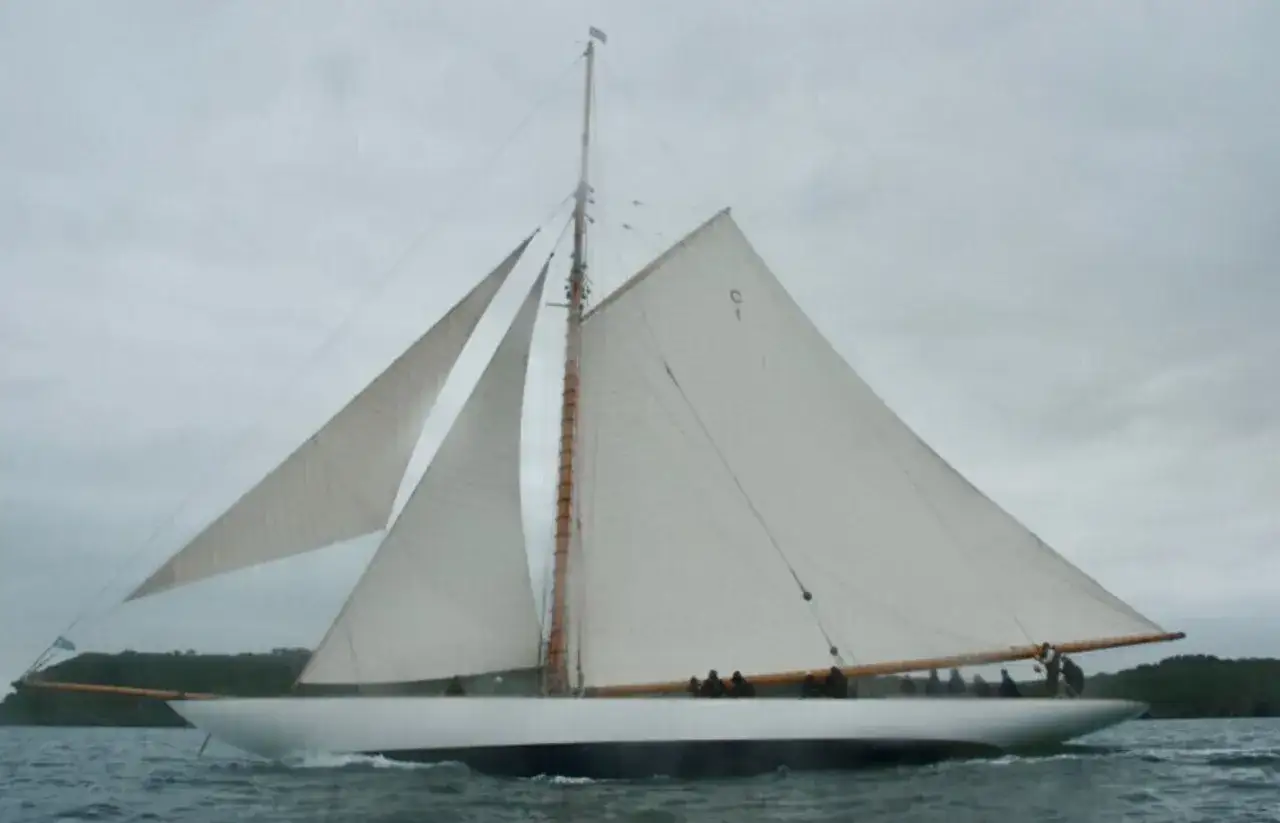 Un voilier majestueux, une mariquita, navigue sur des eaux calmes sous un ciel couvert. Ses voiles blanches sont gonflées par le vent.