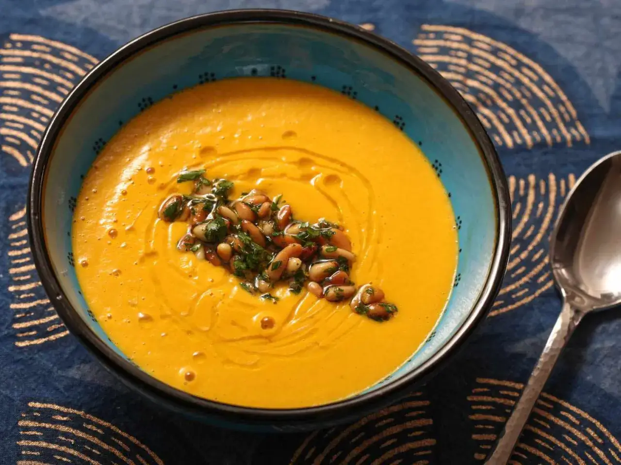 Un taz&oacute;n azul con un cremoso y vibrante **pure de verduras** naranja, adornado con pi&ntilde;ones tostados y perejil picado.