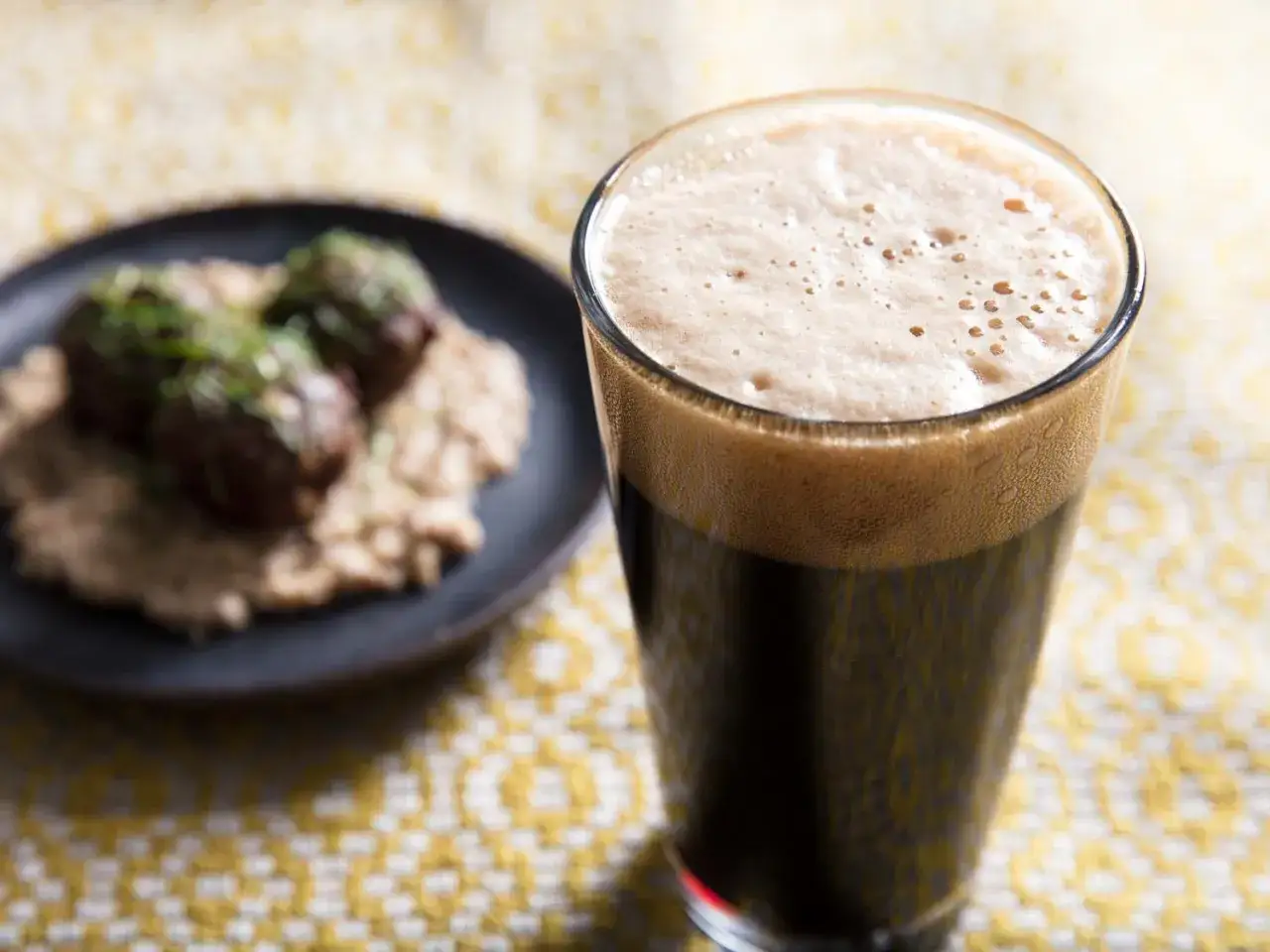 Gęsta piana na ciemnym piwie stout, obok talerz z klopsikami na puree. Idealne połączenie smaków.