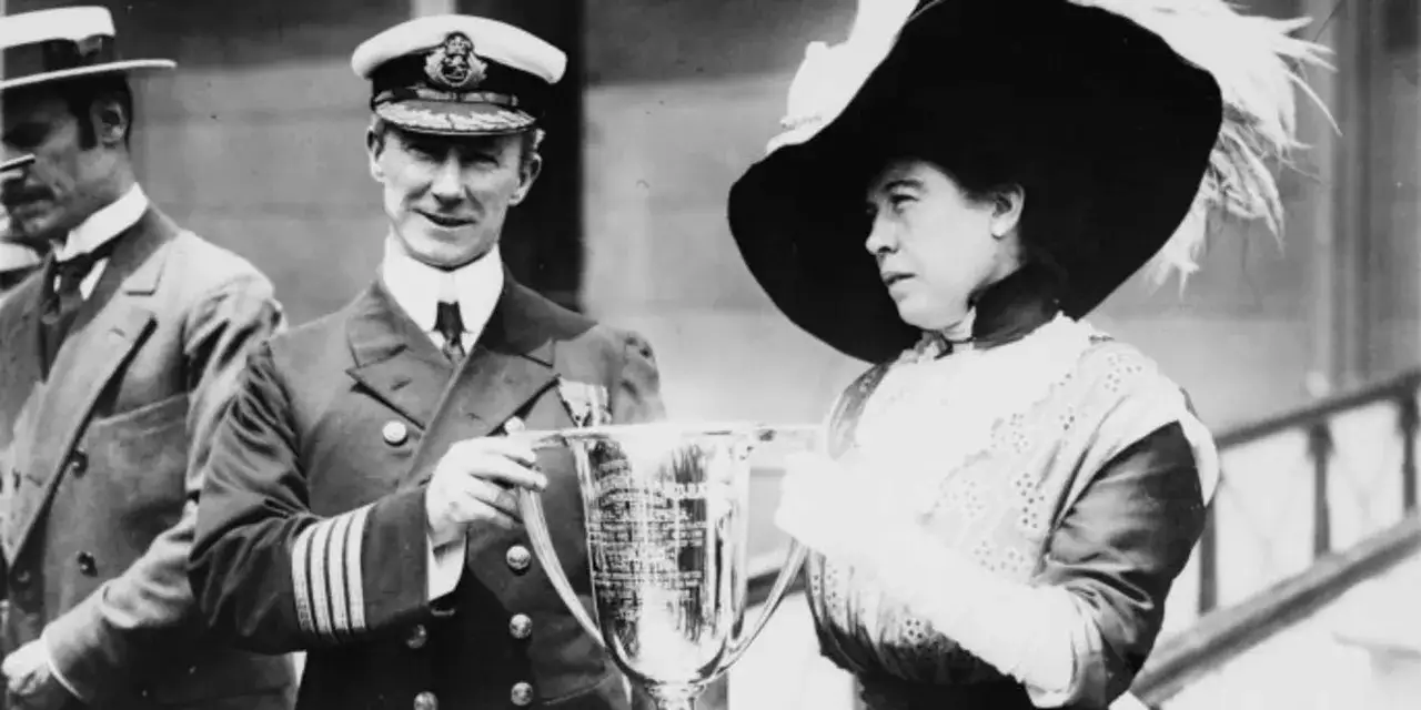 Oficial y dama, supervivientes del Titanic, sostienen un trofeo.