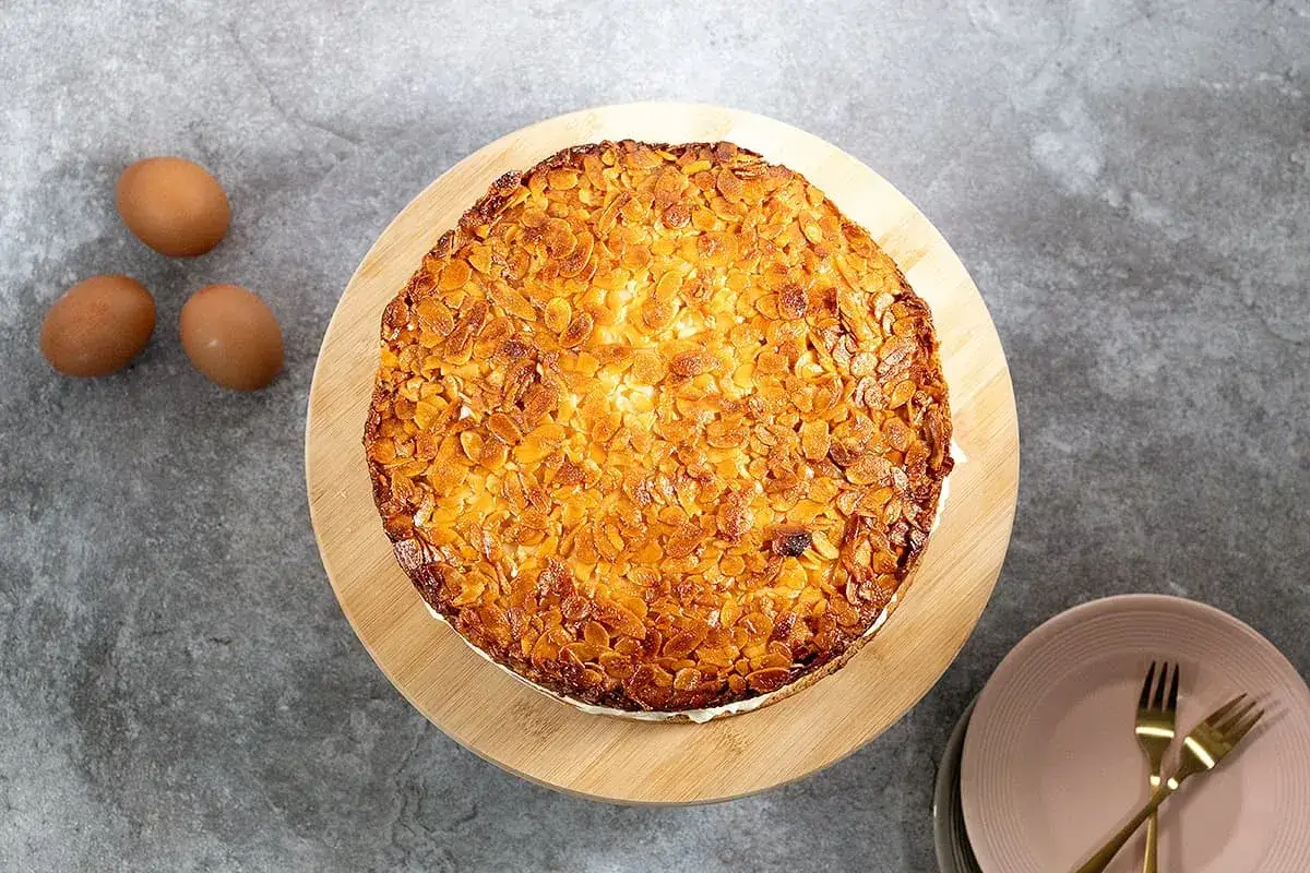 Un délicieux gâteau nid d'abeille, recouvert d'amandes grillées, est prêt à être dégusté. Trois œufs bruns sont posés à côté.