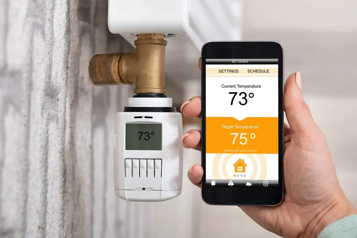 Une main tient un smartphone affichant un cee thermostat connect&eacute;. La temp&eacute;rature actuelle est de 73&deg;, la cible est de 75&deg;.
