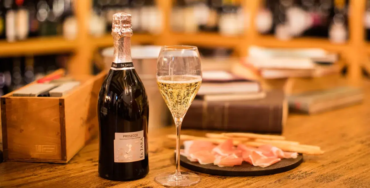 Butelka i kieliszek musującego **prosecco** obok przekąsek.